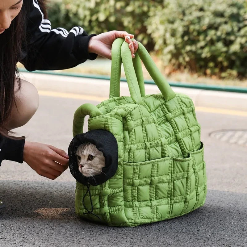 Person holding a green quilted handbag with a small black bag inside containing a cat.